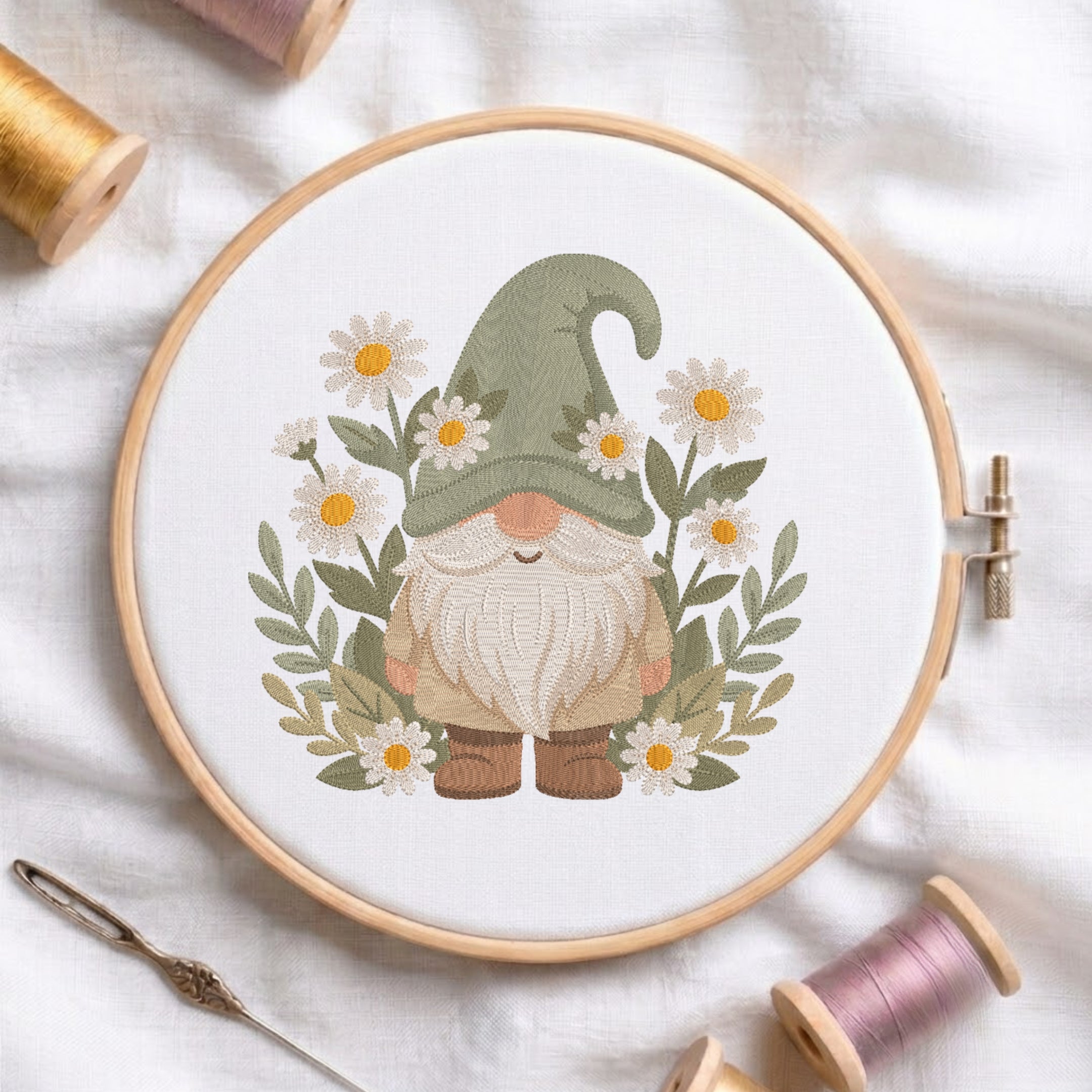 A circular embroidery hoop holding white fabric with a stitched gnomes design surrounded by daisies and green leaves. The hoop is styled on a white fabric background with spools of thread, a needle, and wooden pegs.