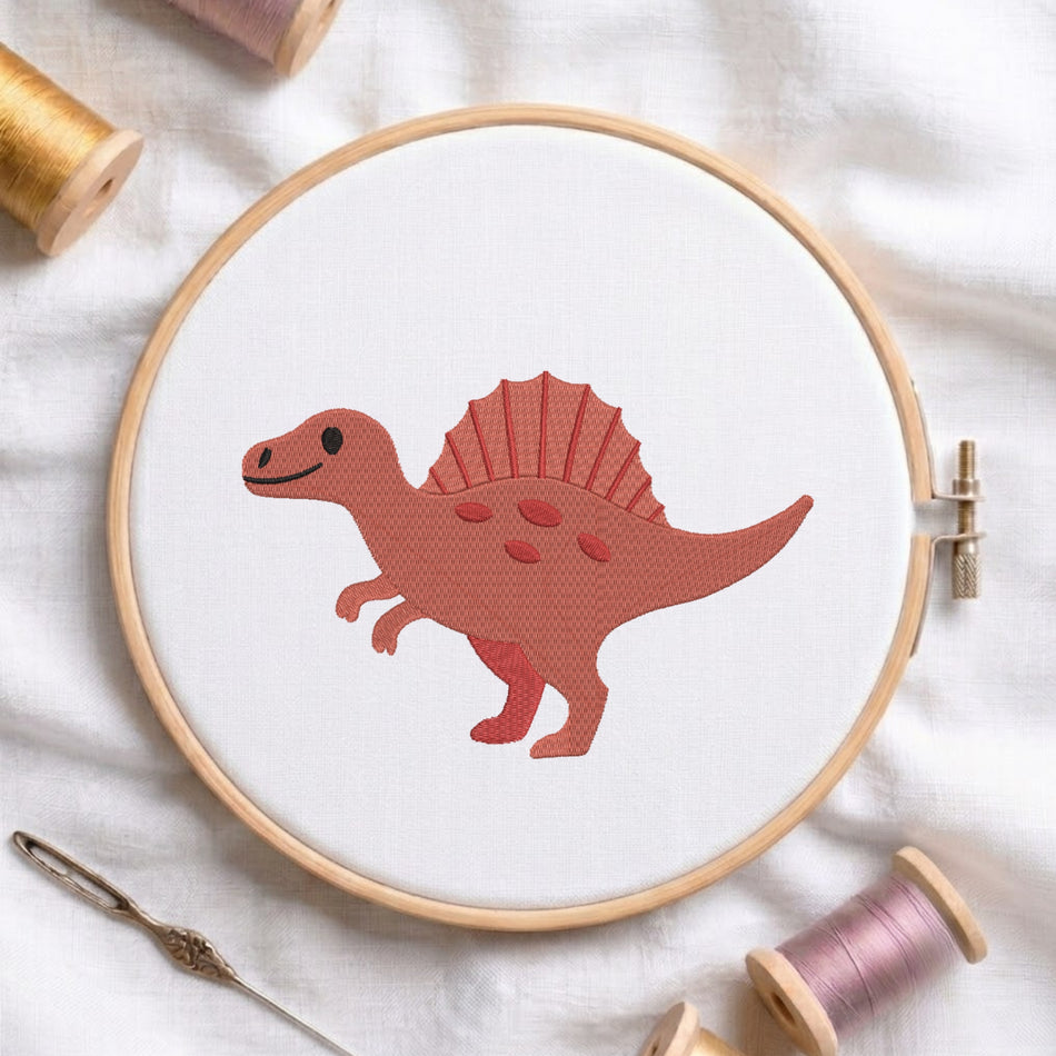 A wooden embroidery hoop holds white fabric with a stylized red dinosaur design in the center. Surrounding props include spools of thread, a needle, and soft white fabric, arranged in a styled flat-lay.