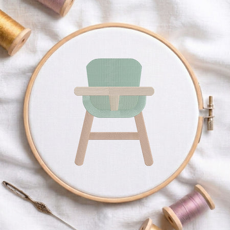 An embroidered baby high chair design with a green seat and beige wooden legs, stitched inside a wooden hoop on white fabric with sewing threads.