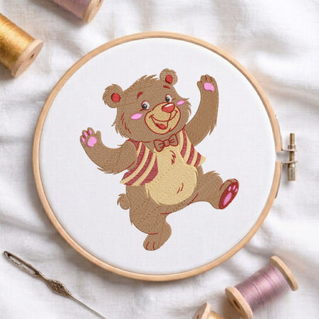 An embroidered dancing bear design displayed in a wooden embroidery hoop, with a needle and thread spools nearby.