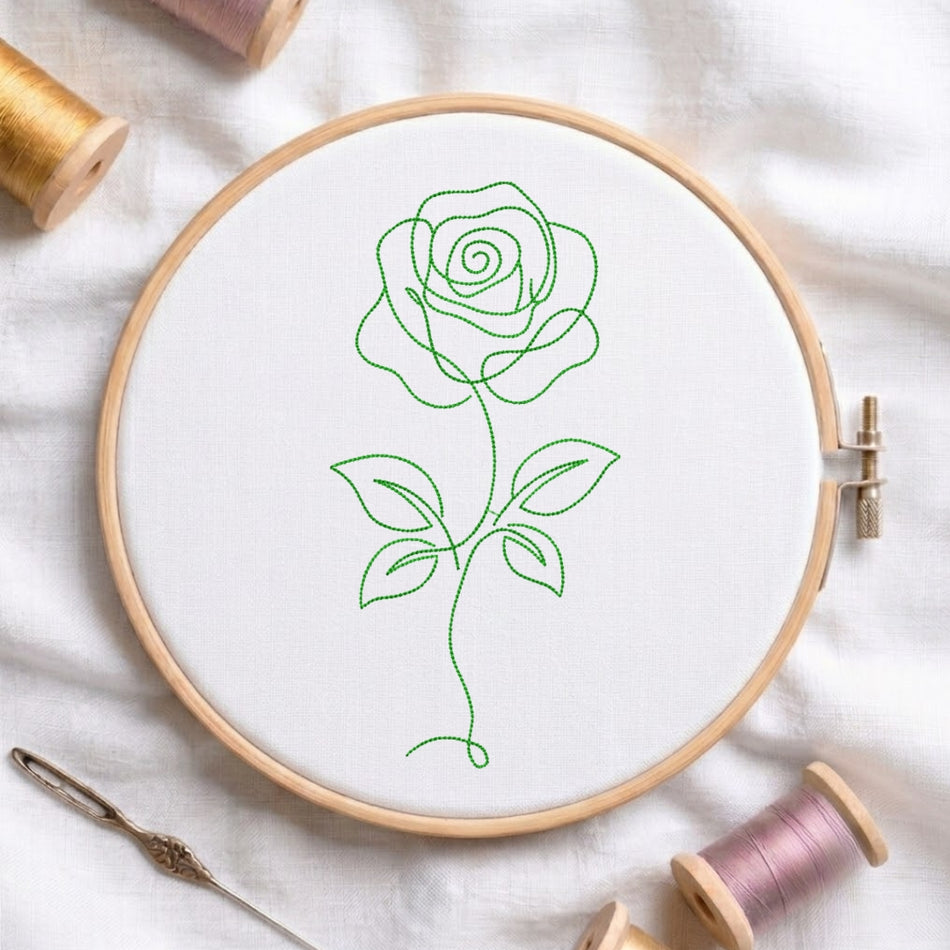 A green continuous line art rose machine embroidery design stitched on white fabric inside a wooden embroidery hoop, surrounded by embroidery thread spools.