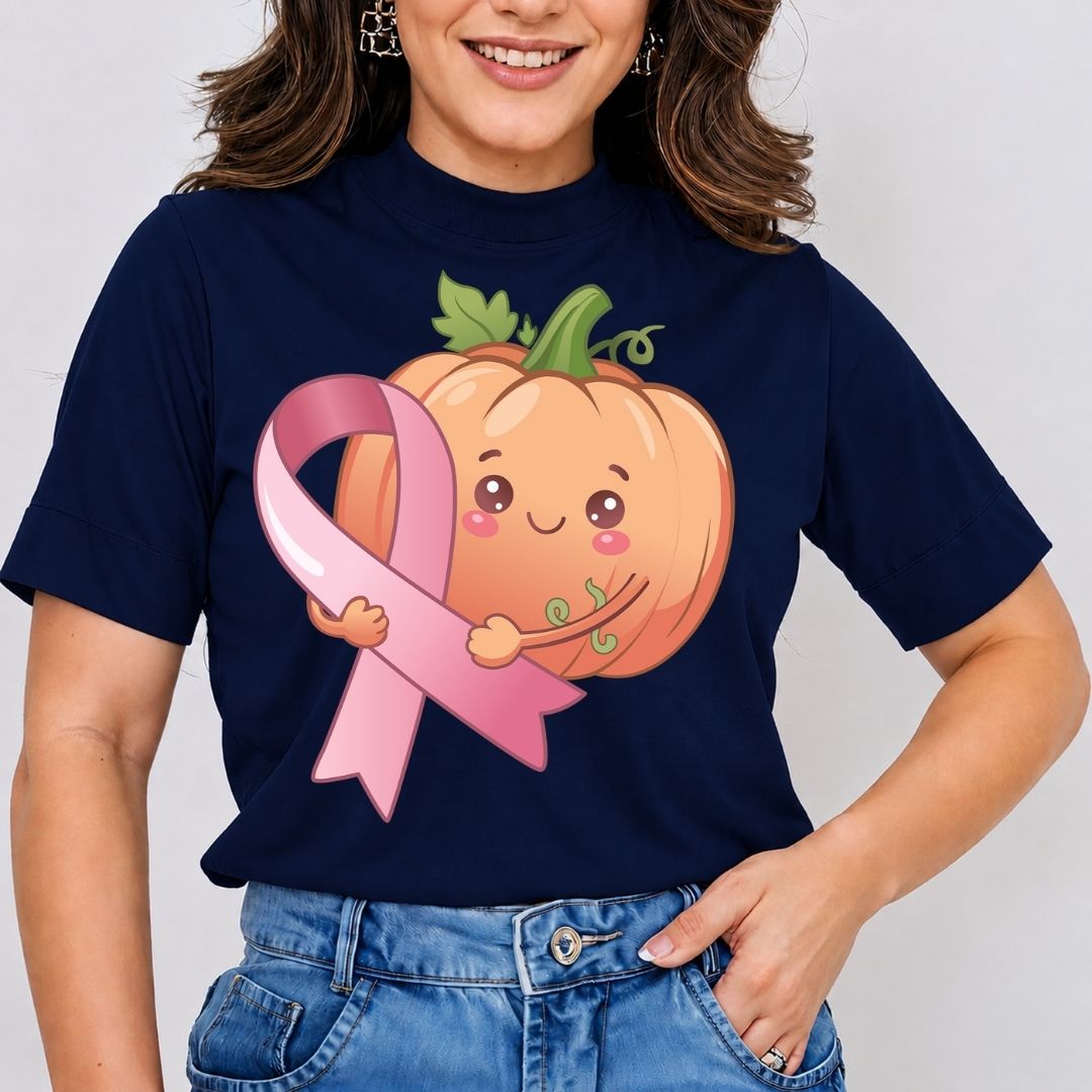 A woman wearing a navy blue t-shirt with a cute graphic of a smiling orange pumpkin holding a pink breast cancer awareness ribbon. She is also wearing blue jeans, photographed against a light gray background.