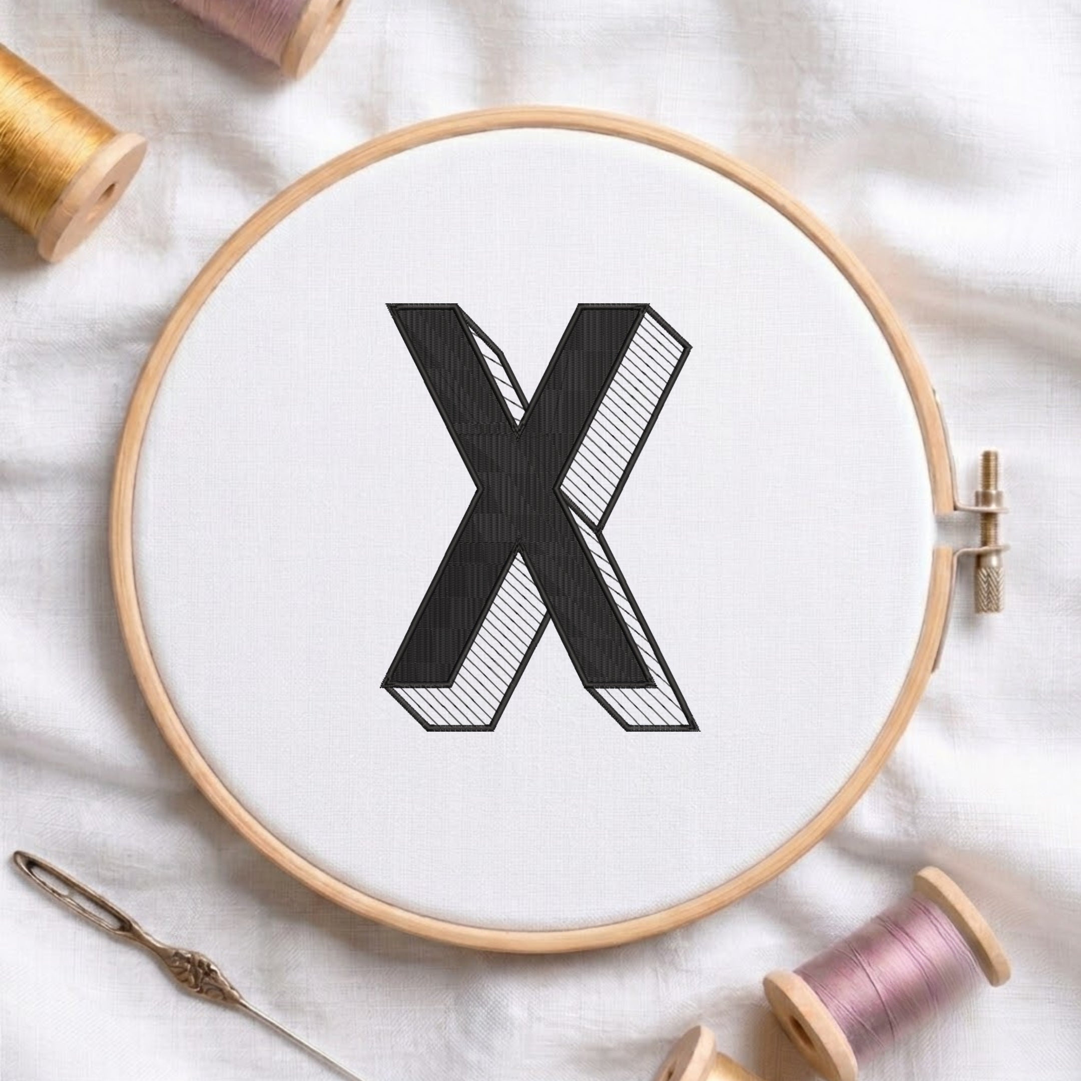 A wooden embroidery hoop holding white fabric with a large black letter X stitched in the center, surrounded by spools of thread and a needle on a white fabric background.