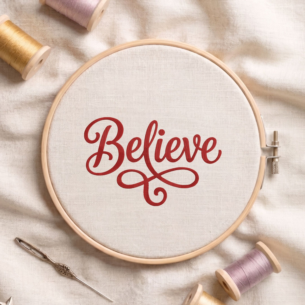 "Believe" word art machine embroidery design with elegant cursive lettering displayed inside a round wooden hoop on white linen fabric, accompanied by wooden thread spools and a needle.