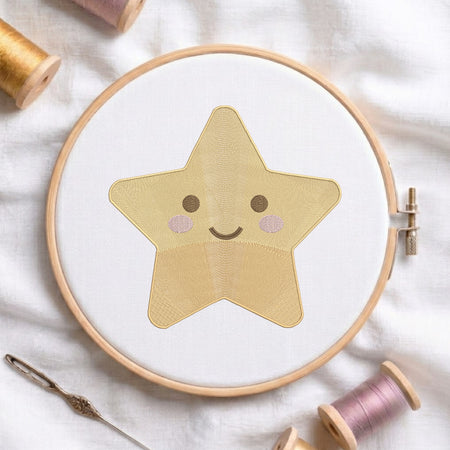 A star-shaped embroidered patch with a smiling face, stitched in a light wood hoop on white fabric, surrounded by spools of thread and a needle on a white textured background.
