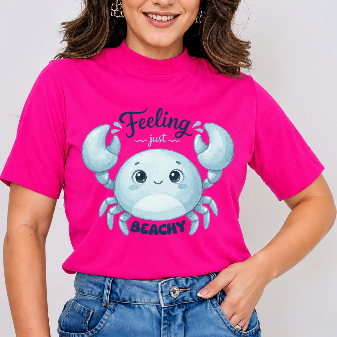 A person wearing a bright hot-pink t-shirt featuring a blue cartoon crab graphic and the text "Feeling just BEACHY".