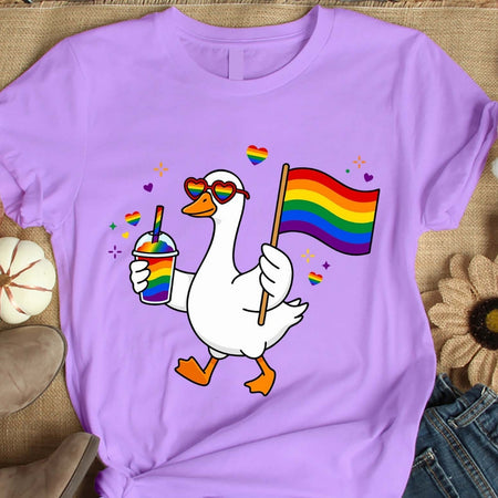 Purple t-shirt with a cartoon duck holding a rainbow flag and drink, on a textured surface.