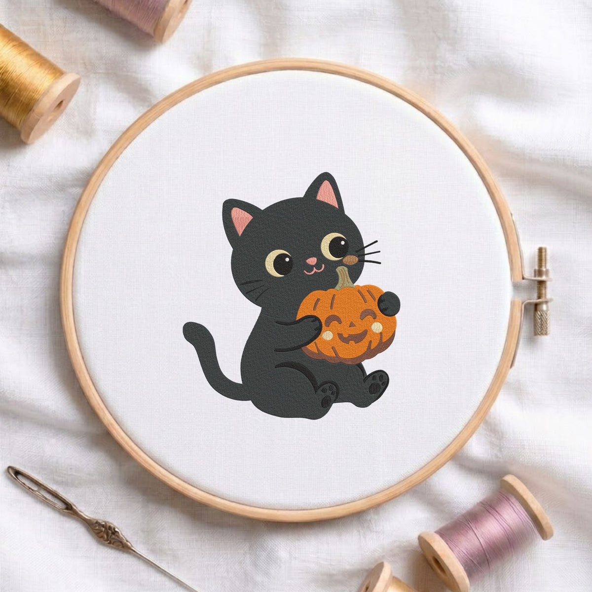 Cute black cat hugging a mini jack-o-lantern pumpkin Halloween machine embroidery design shown in a wooden embroidery hoop on white fabric with thread spools and a needle