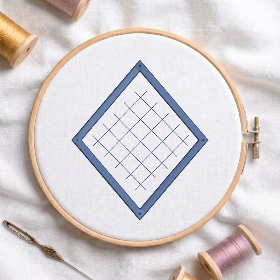A wooden embroidery hoop holding white fabric with a blue diamond grid design, styled on a white cloth with spools of thread and a needle around it.