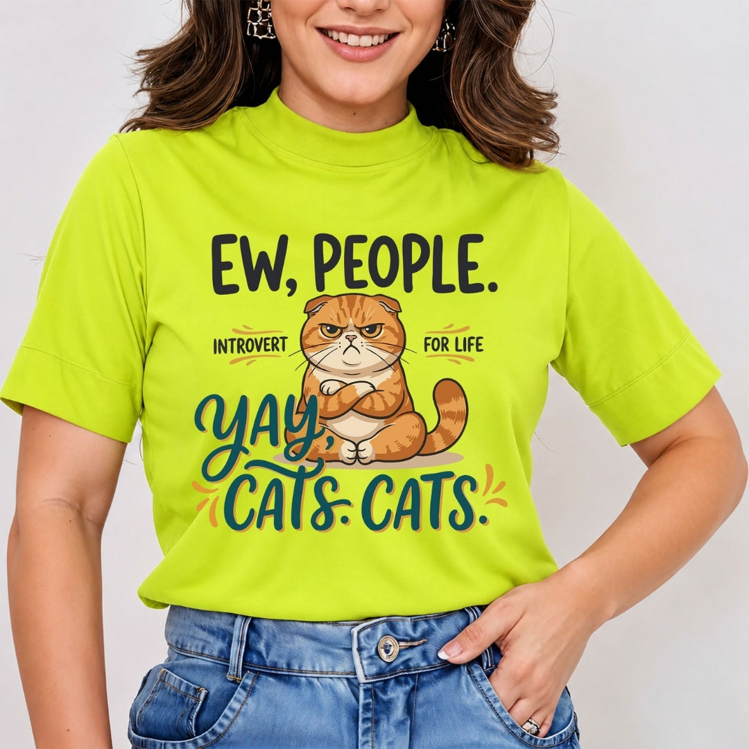 Woman wearing a bright lime green mock neck t-shirt featuring a funny cartoon illustration of a grumpy orange cat with arms crossed and the text "Ew, People. Introvert for Life. Yay, Cats. Cats.", tucked into blue jeans.