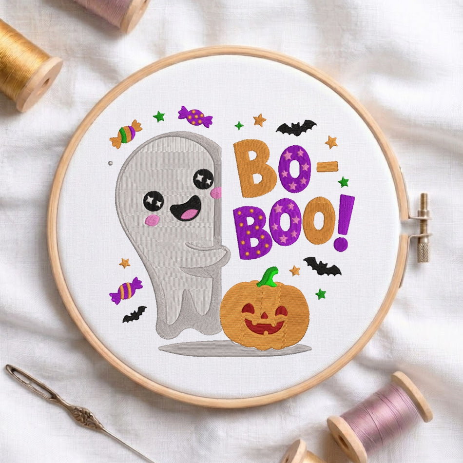 The "Bo-Boo!" embroidery design centered in a wooden embroidery hoop, surrounded by embroidery thread spools and a needle.