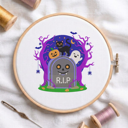 A circular embroidery hoop holding white fabric with a colorful Halloween-themed stitched design: a gray tombstone reading R.I.