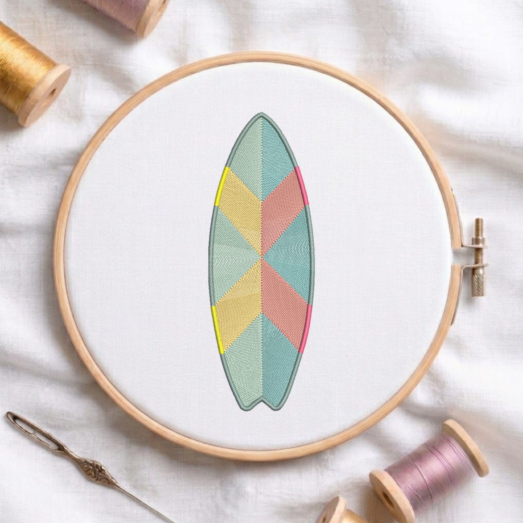 A wooden embroidery hoop holds white fabric with a surfboard-shaped geometric embroidery design in pastel teal, pink, yellow, and sage green. The hoop is styled on a white fabric background with spools of thread and a needle nearby.