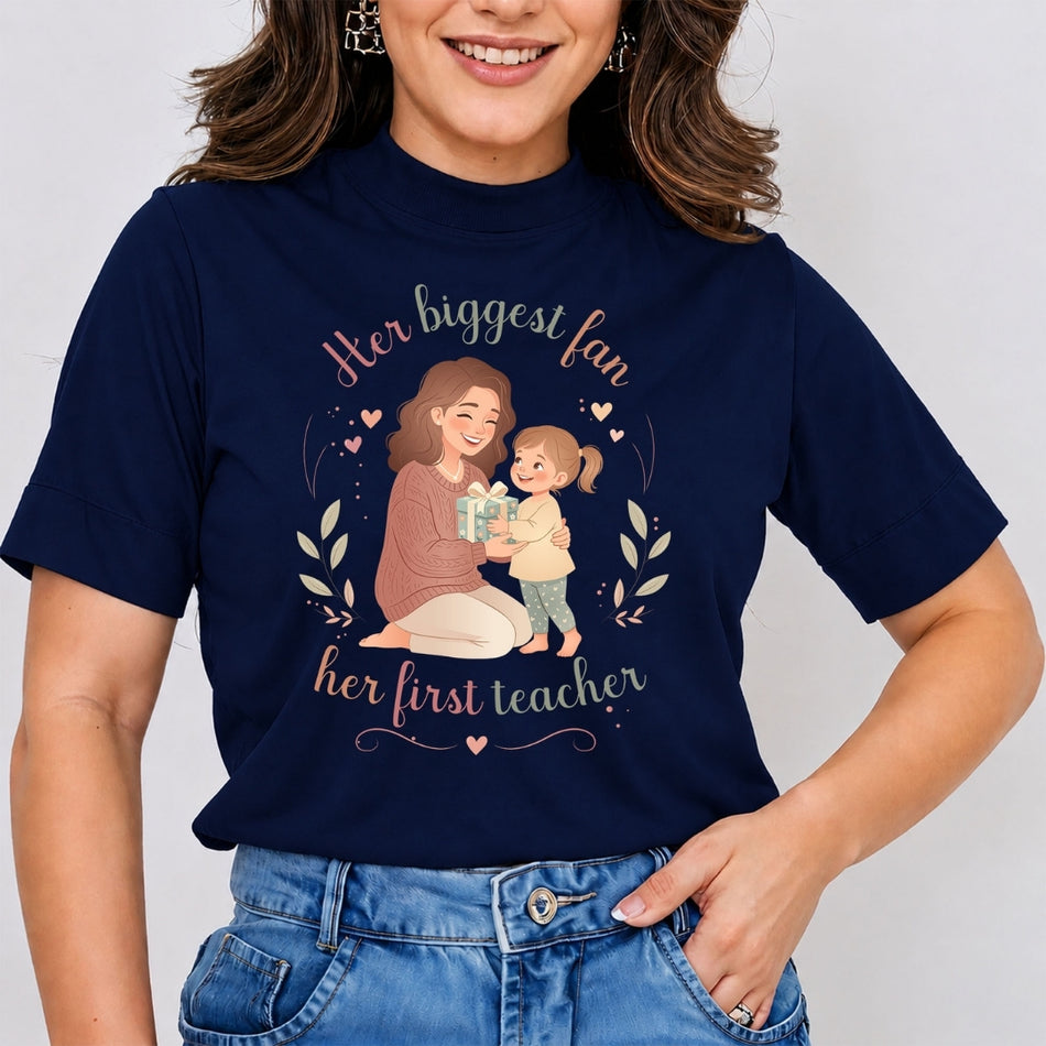Woman wearing a dark navy blue mock neck t-shirt featuring a Mother's Day graphic of a mother receiving a gift from her daughter, with text reading Her biggest fan, her first teacher.