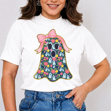A woman wearing a white short-sleeve t-shirt with a colorful graphic of a cute ghost character, styled with blue jeans against a plain light gray background.