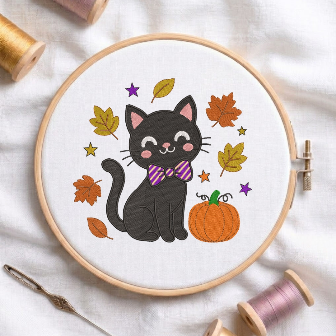 A circular embroidery hoop on white fabric, featuring a black cat wearing a purple striped bow tie, surrounded by autumn leaves, stars, and an orange pumpkin. Spools of thread and a needle are arranged around the hoop.
