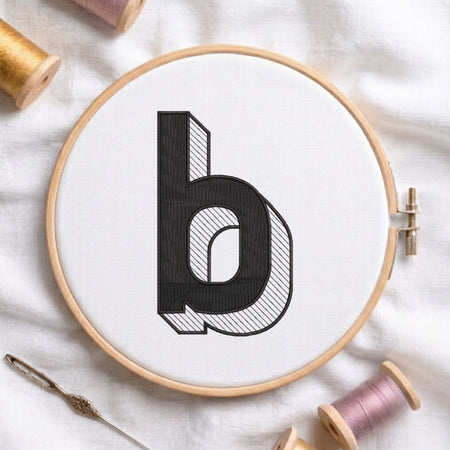 An embroidered 3D block lowercase letter "b" with striped shading texture, stitched inside a wooden hoop on white fabric with sewing threads.