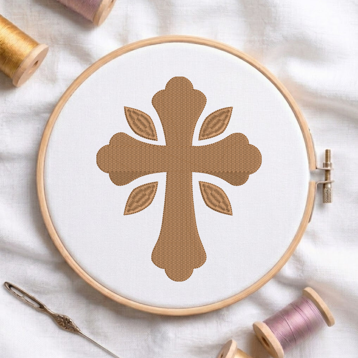Soft gold ornamental cross pattern with four leaf accents embroidered on white fabric inside a wooden hoop.