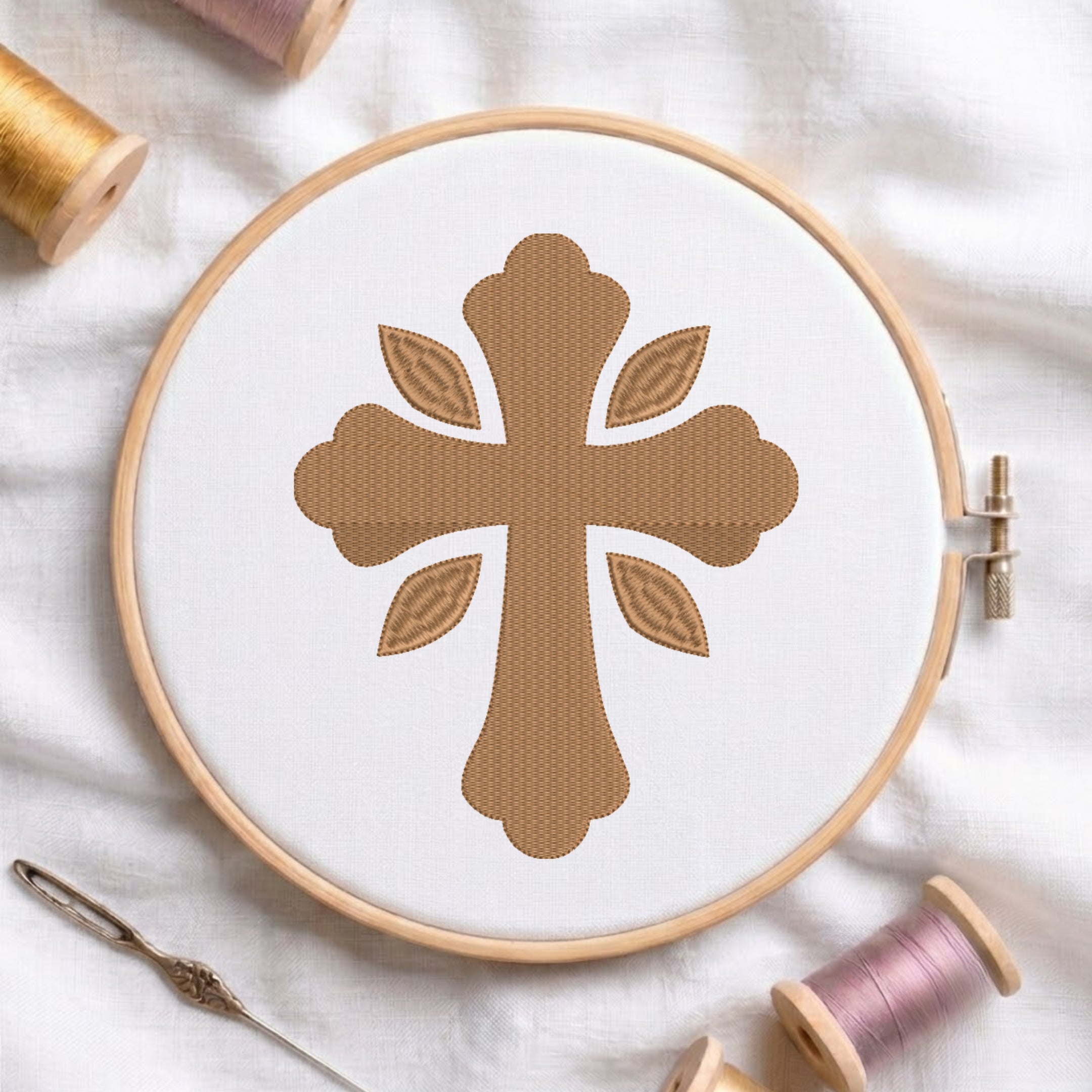 Soft gold ornamental cross pattern with four leaf accents embroidered on white fabric inside a wooden hoop.