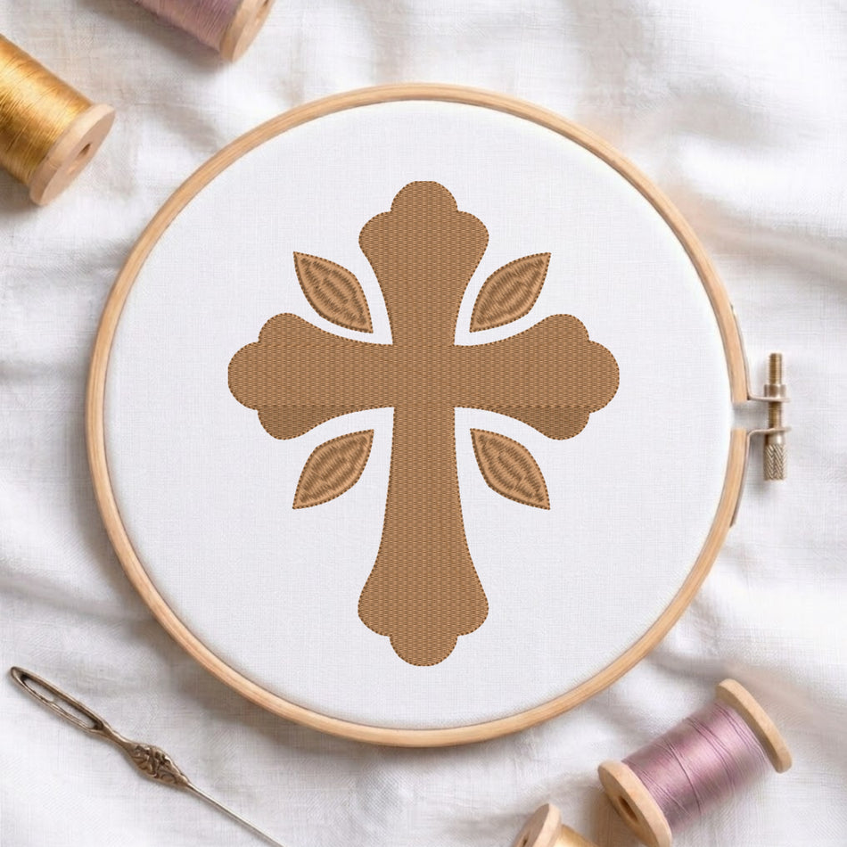 Soft gold ornamental cross pattern with four leaf accents embroidered on white fabric inside a wooden hoop.
