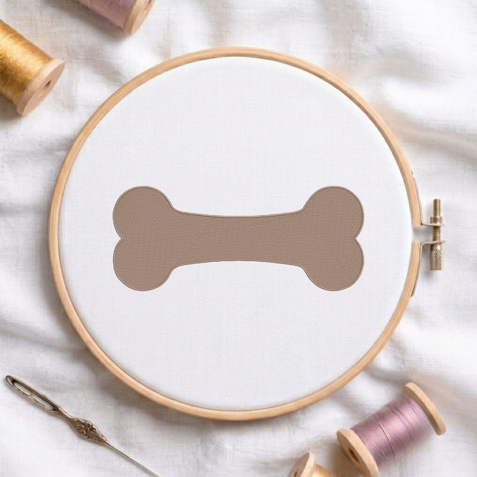 A circular embroidery hoop holding white fabric with a large taupe bone shape stitched in the center, styled on a white fabric background with thread spools and a needle around it.