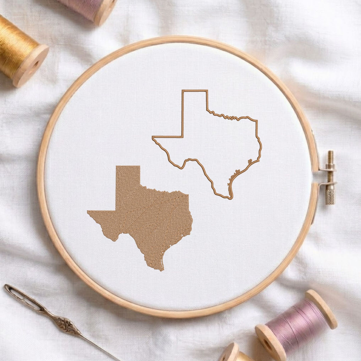 A wooden embroidery hoop holds white fabric with two embroidered Texas-shaped outlines in tan thread, surrounded by spools of thread and a needle on a white fabric background.