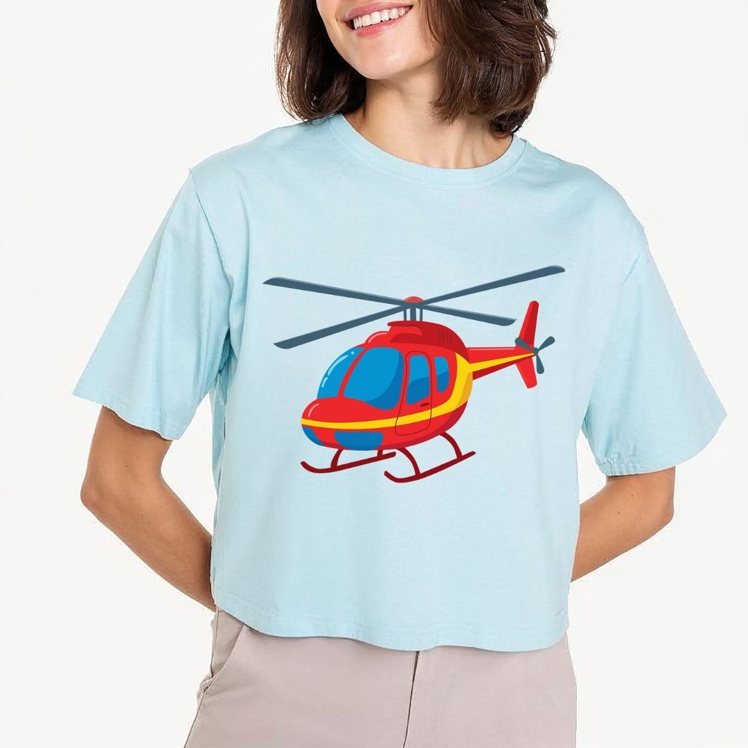 A woman wearing a light blue cropped t-shirt with a cartoon helicopter graphic on the front, paired with beige pants, against a plain light background.