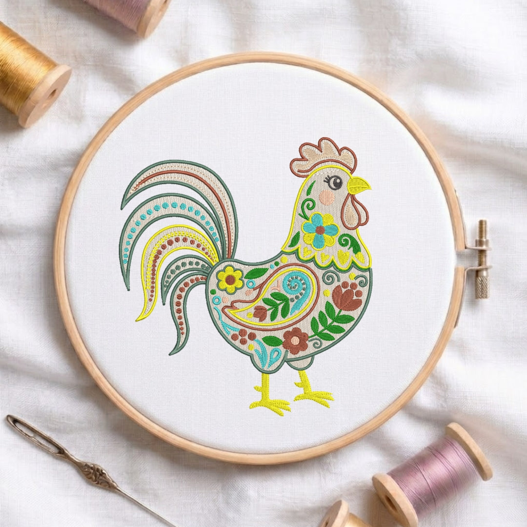 A round embroidery hoop holding white fabric with a colorful embroidered rooster design. The rooster illustration features yellow, green, blue, red, and brown floral and geometric patterns.