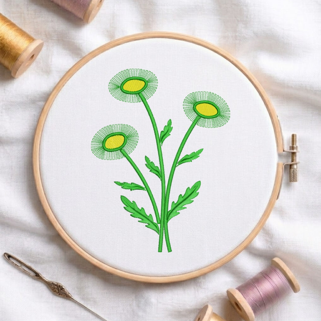 A circular embroidery hoop holding white fabric with a green and yellow flower design, surrounded by spools of thread and a needle on a white fabric background.
