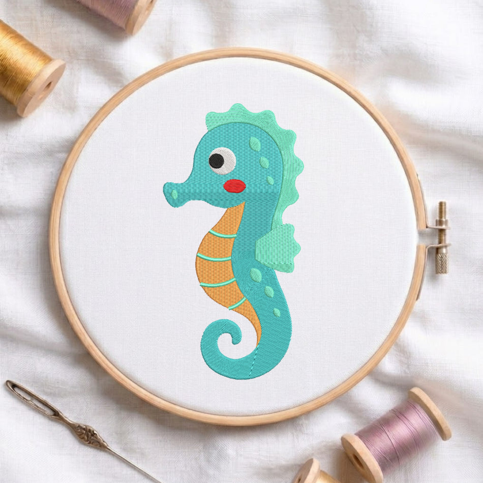A wooden embroidery hoop on white fabric, featuring a colorful stitched seahorse design in teal, orange, and red. Surrounding props include spools of thread and a needle on a soft white cloth background.