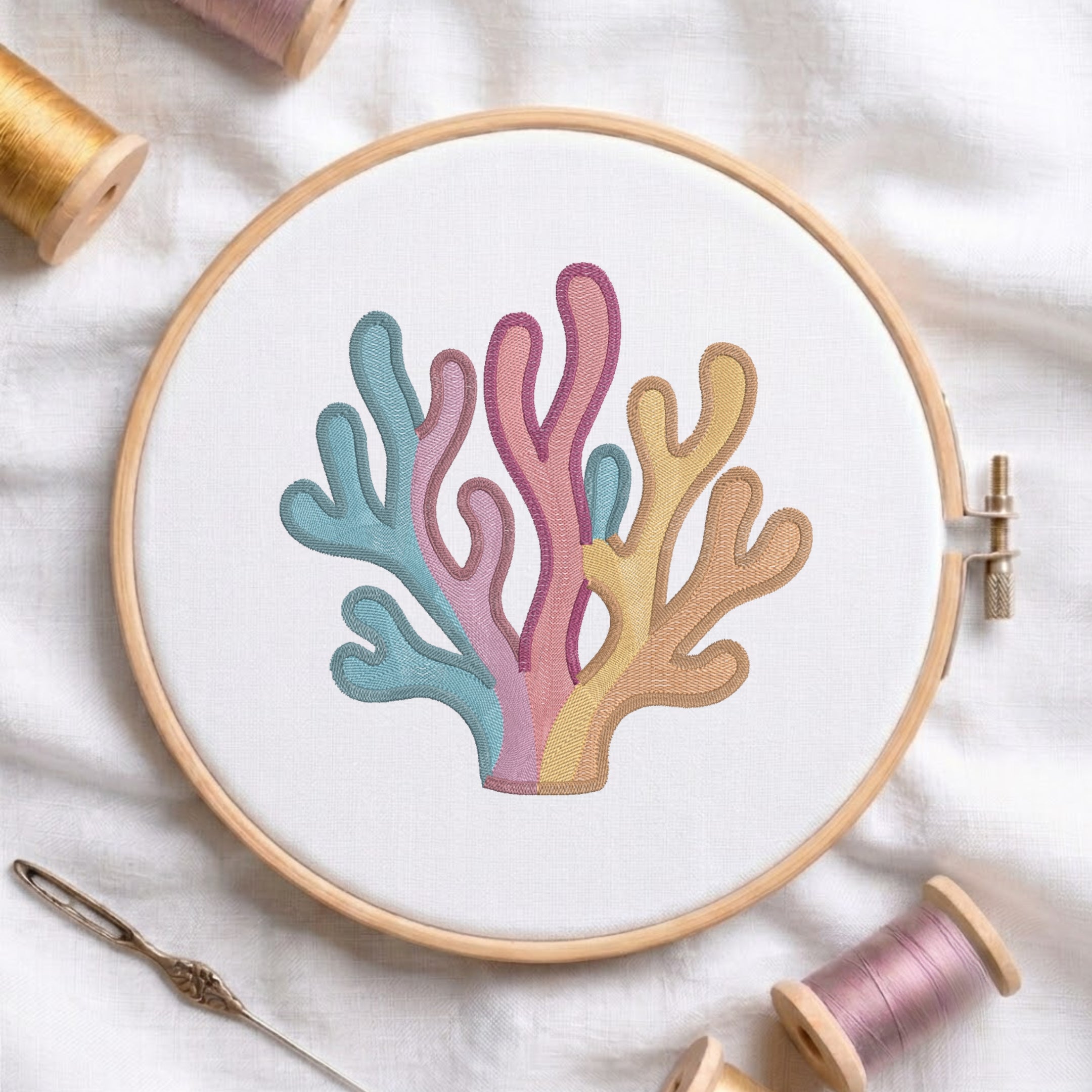 A coral embroidery design stitched inside a wooden embroidery hoop, surrounded by spools of thread and a needle on a white fabric background.