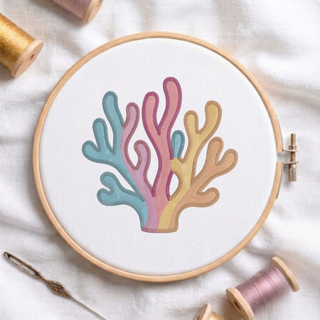 A coral embroidery design stitched inside a wooden embroidery hoop, surrounded by spools of thread and a needle on a white fabric background.