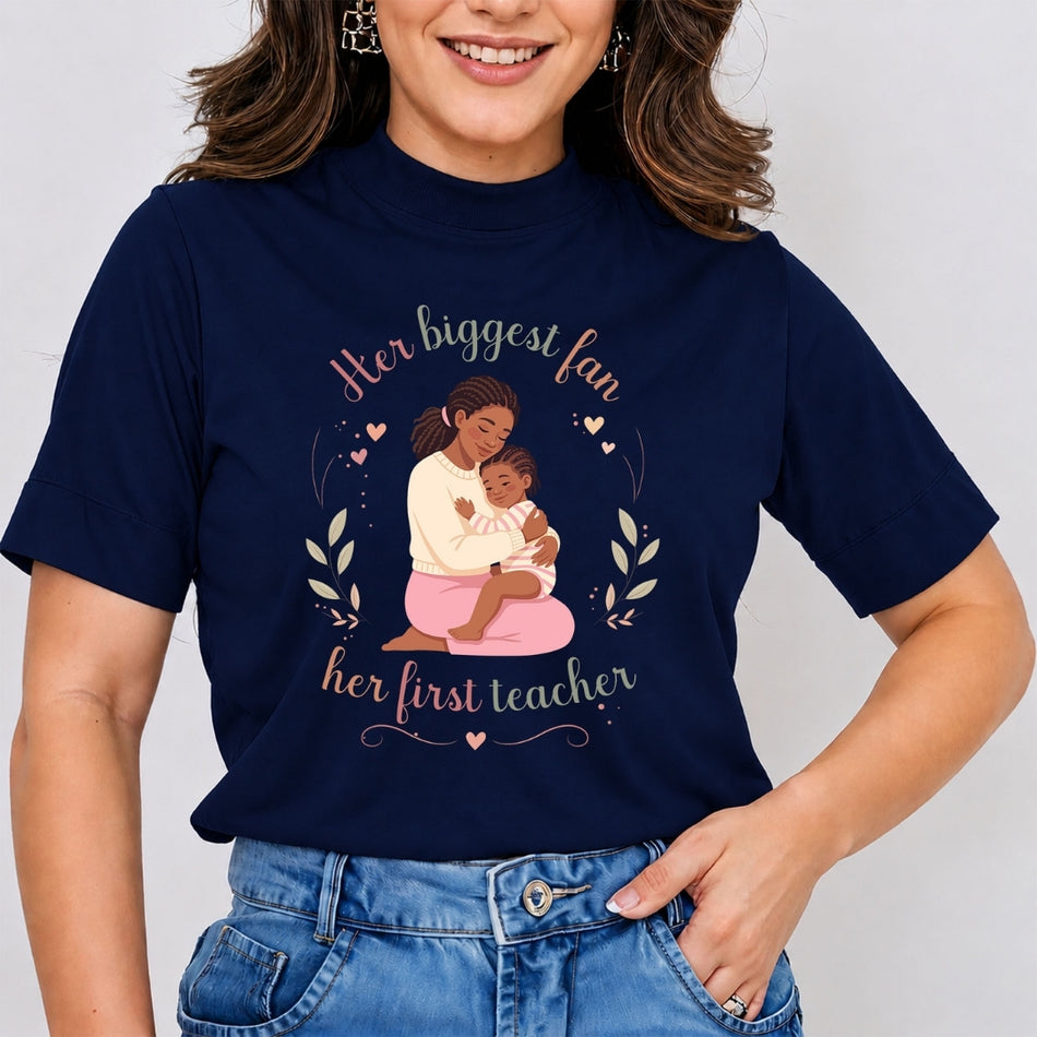Woman wearing a dark navy blue mock neck t-shirt featuring a Mother's Day graphic of a mother receiving a gift from her daughter, with text reading Her biggest fan, her first teacher.