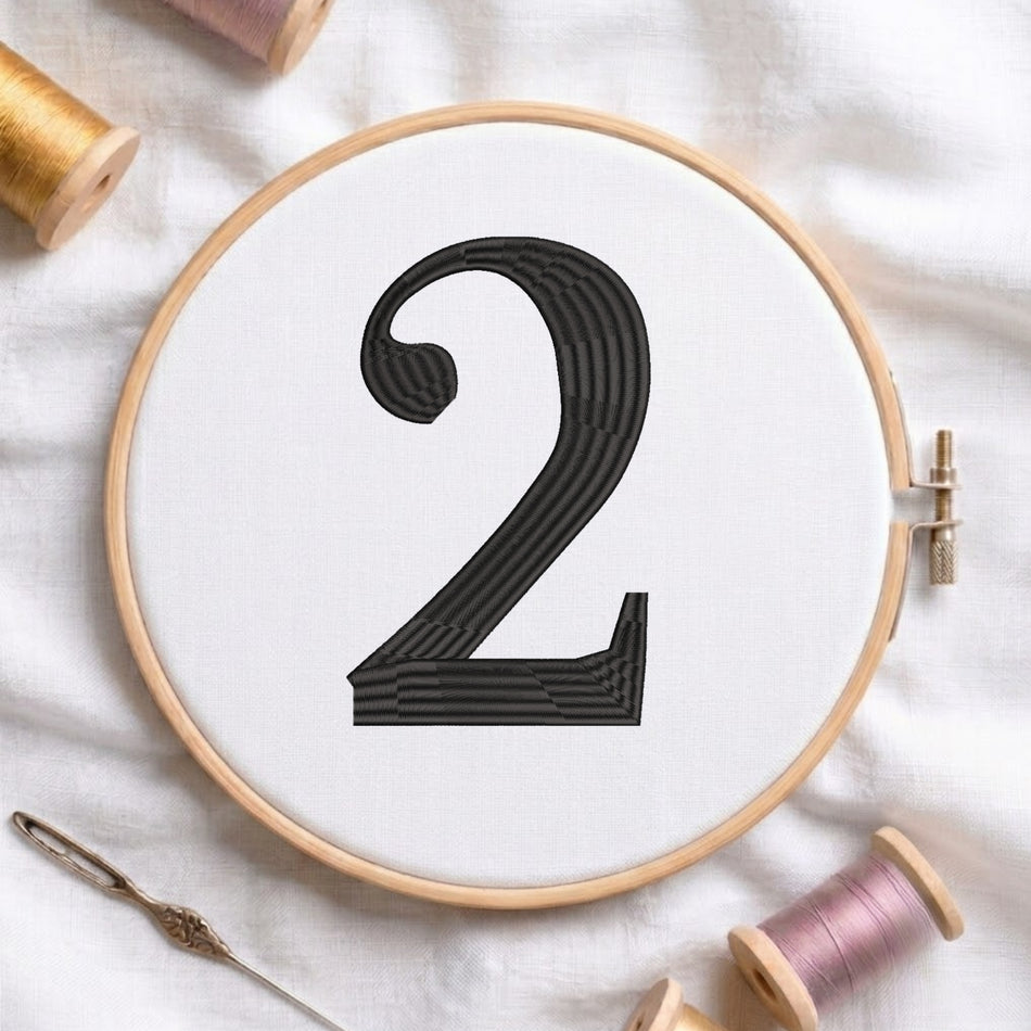 A wooden embroidery hoop holds white fabric with a large black stitched number 2. A needle and thread spools are arranged around it on a white fabric background.