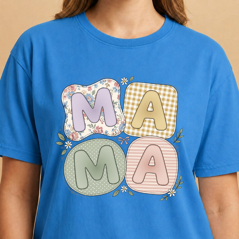 Smiling person wearing a bright blue t-shirt featuring the pastel patchwork "MAMA" graphic and floral details.