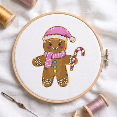 A circular embroidery hoop holding white thread and a gingerbread person design, surrounded by spools of thread and a needle on a white fabric background.