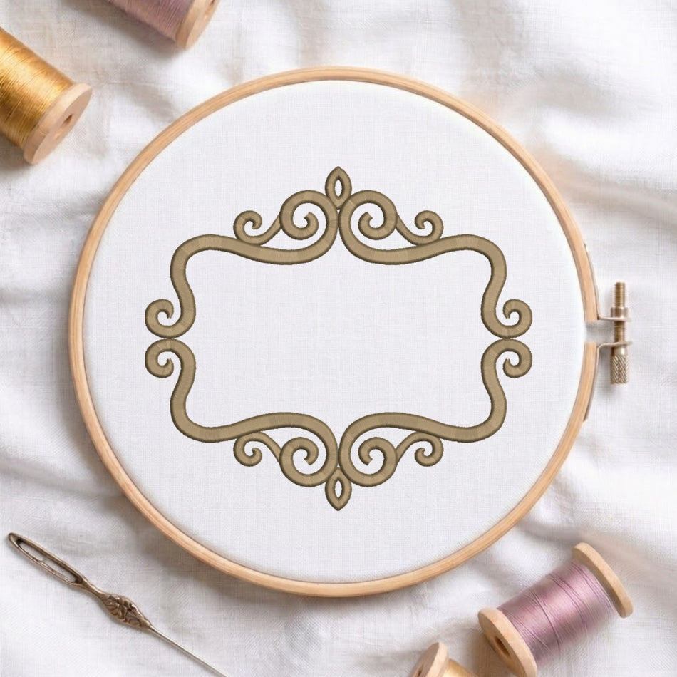 A round embroidery hoop holding white fabric with a decorative gold scrollwork design, styled on a white cloth with thread spools and a needle around it.