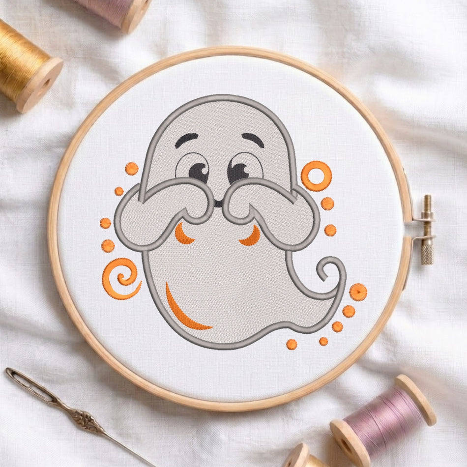 A circular embroidery hoop holding white fabric with a cartoon ghost design in gray and orange, surrounded by spools of thread and a needle on a white fabric background.