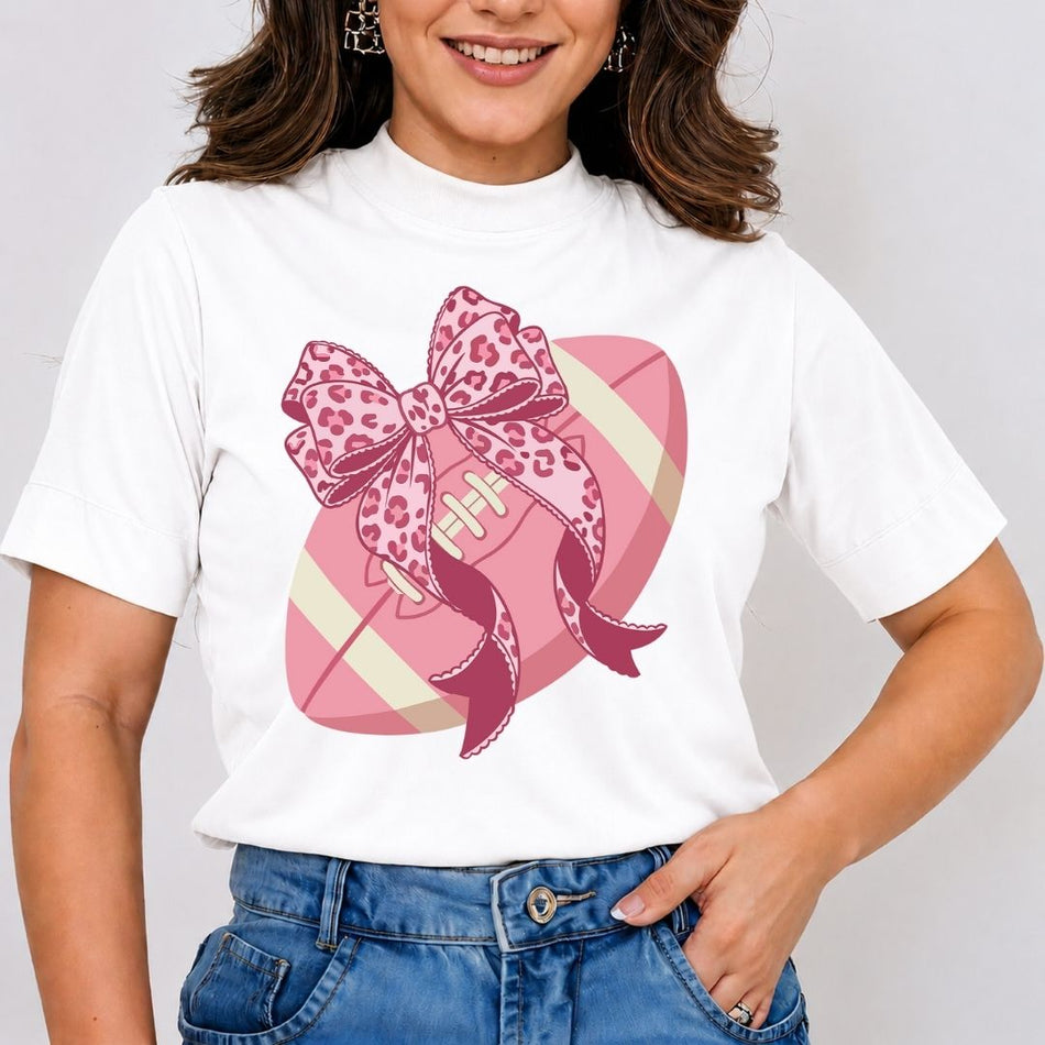 Person wearing a white t-shirt with a pink football and leopard print bow design.