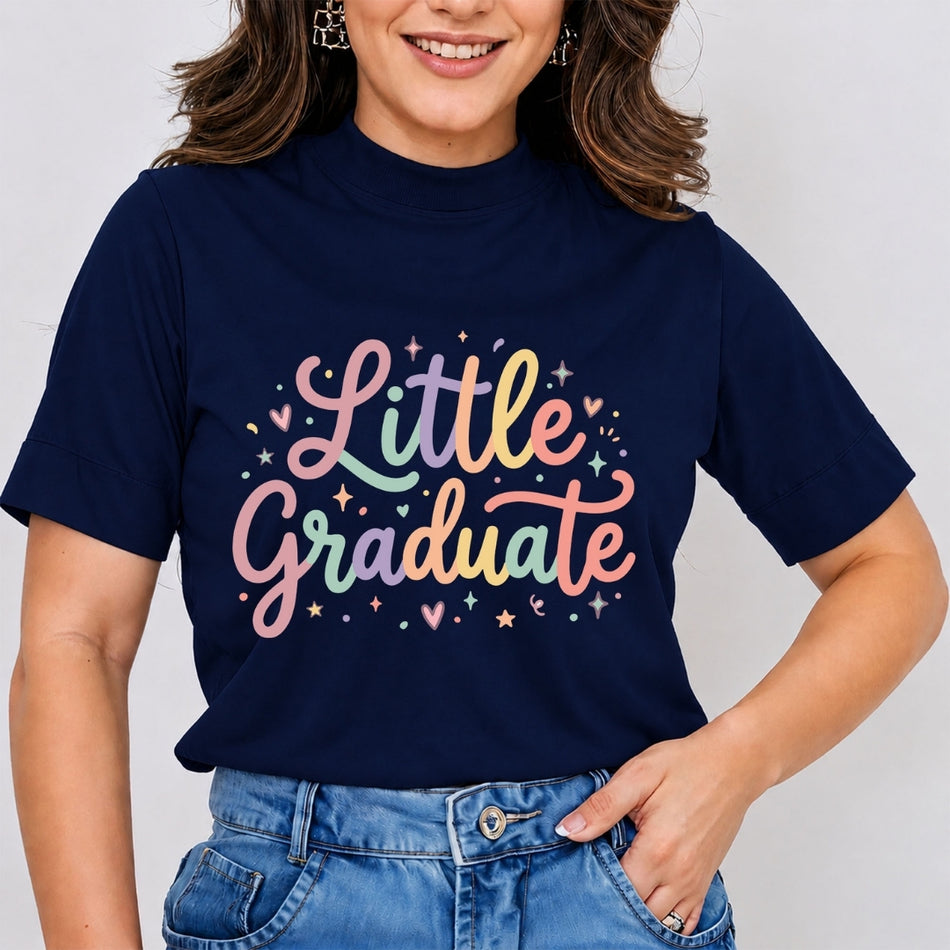A woman wearing a navy blue short-sleeve t-shirt with a colorful pastel graphic that reads 'Little Graduate' in script with stars and hearts, paired with blue jeans against a light gray background.