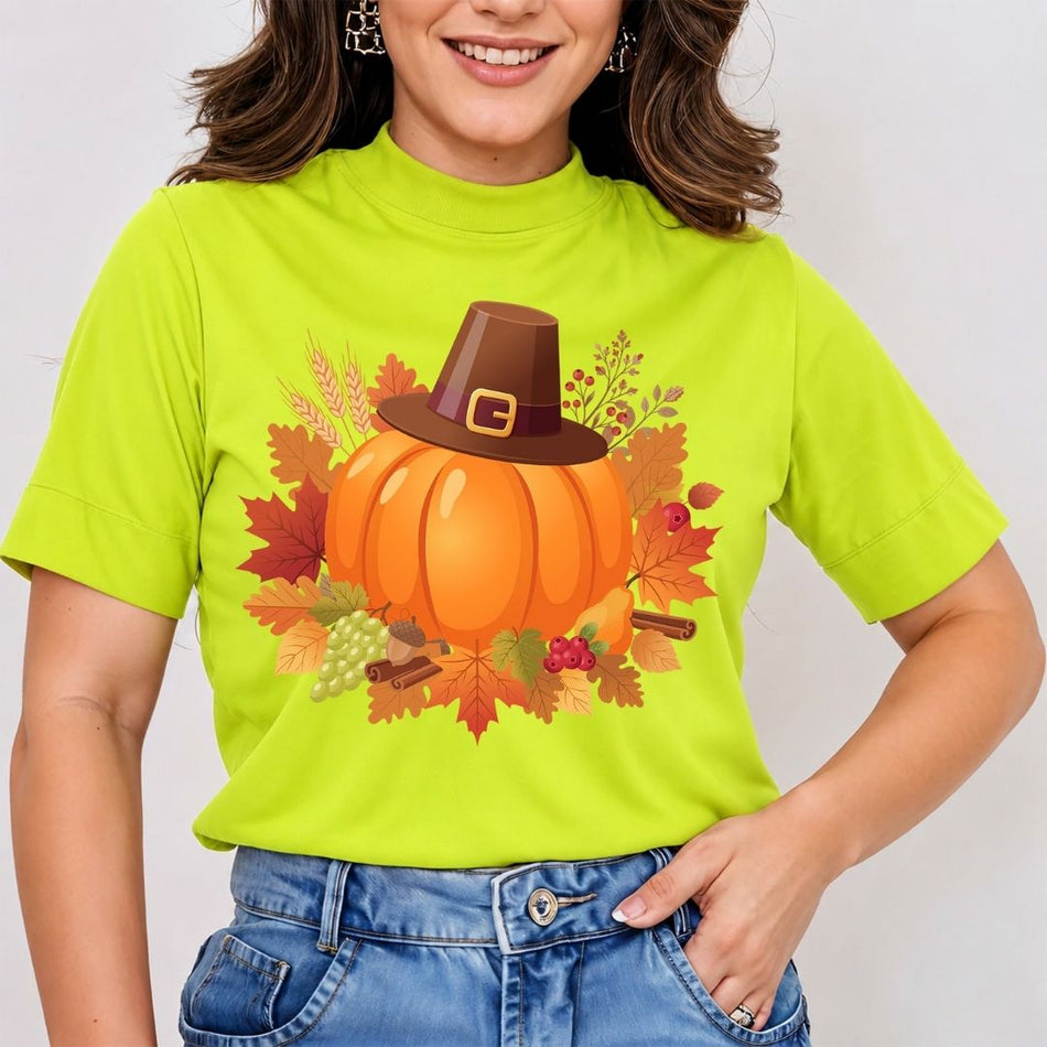 A woman wearing a bright lime green mock-neck t-shirt with a graphic of a pumpkin wearing a brown pilgrim hat surrounded by autumn leaves, set against a plain light gray background.