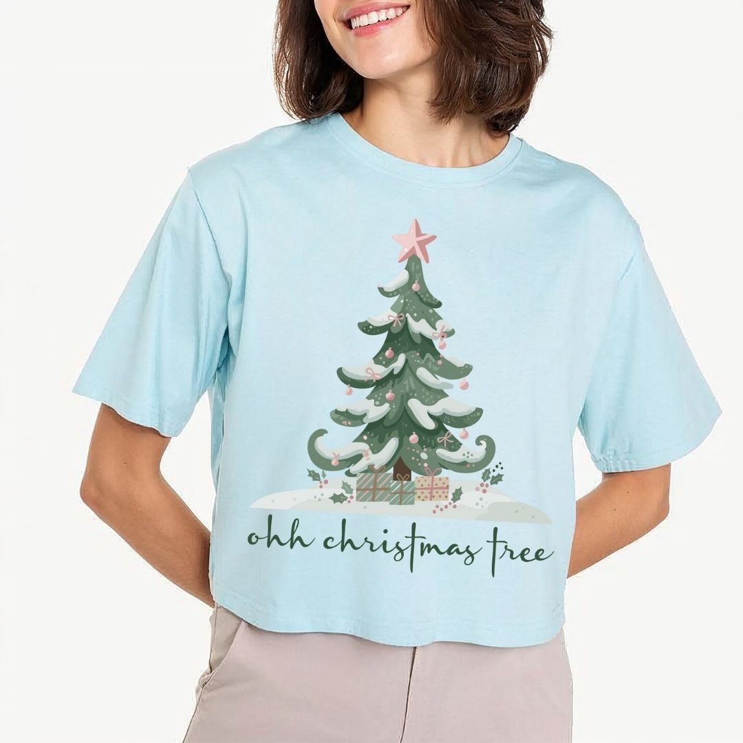 Woman wearing a light blue t-shirt featuring a festive "ohh christmas tree" typography and winter tree graphic design.