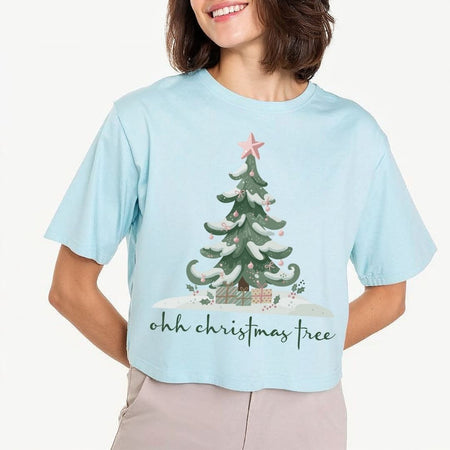 Woman wearing a light blue t-shirt featuring a festive "ohh christmas tree" typography and winter tree graphic design.