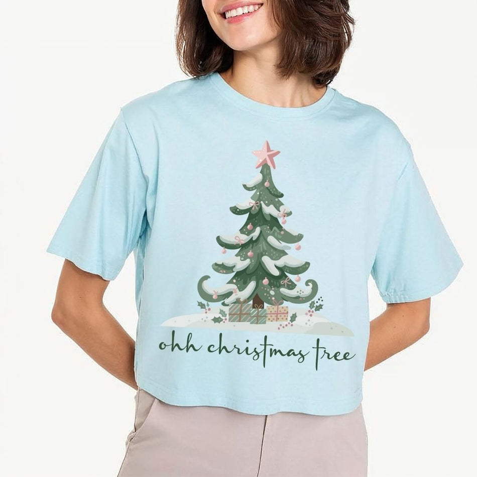 Woman wearing a light blue t-shirt featuring a festive "ohh christmas tree" typography and winter tree graphic design.