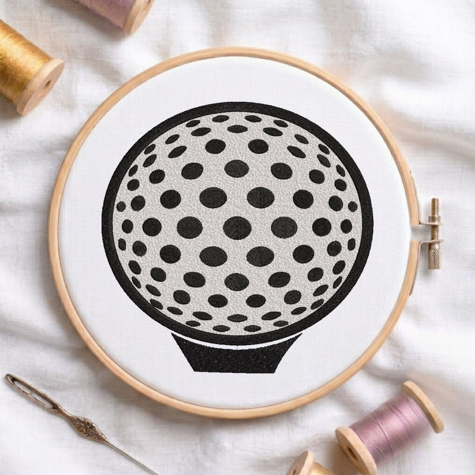 A circular embroidery hoop holding white fabric with a black-and-white polka dot golf ball design, styled on a white cloth with spools of thread and a needle around it.
