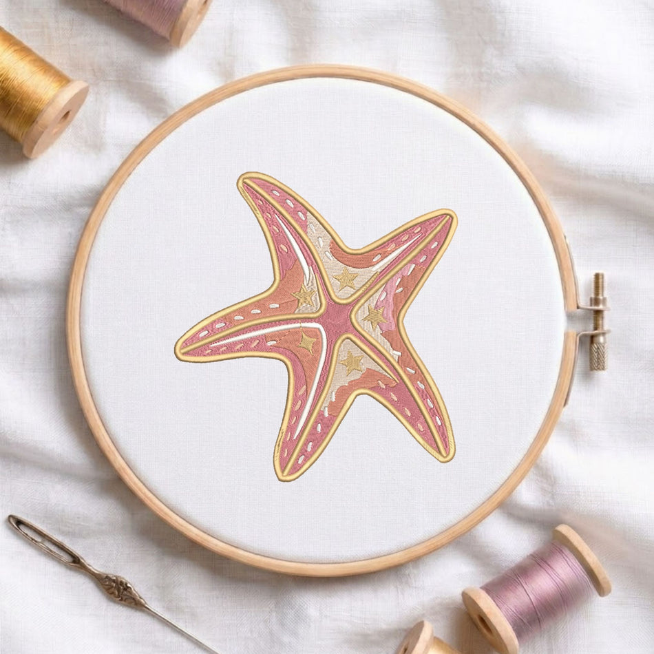 Pink and beige coastal starfish machine embroidery design displayed inside a round wooden hoop on white fabric alongside thread spools and a needle.