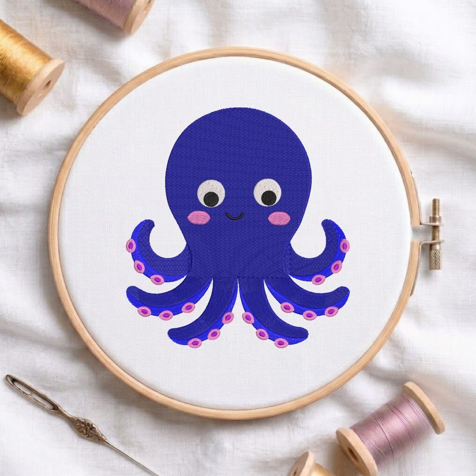 A wooden embroidery hoop holding white fabric with a cartoon octopus design in dark blue, pink, and white. The hoop is styled on a white fabric background with spools of thread and a needle.