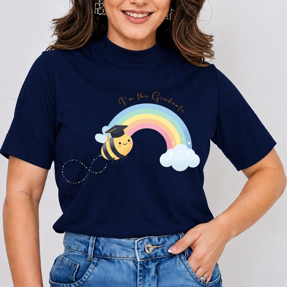 A woman wearing a navy blue short-sleeve t-shirt with a colorful graphic of a graduation bee, rainbow, and clouds with the text 'I'm the Graduate'.