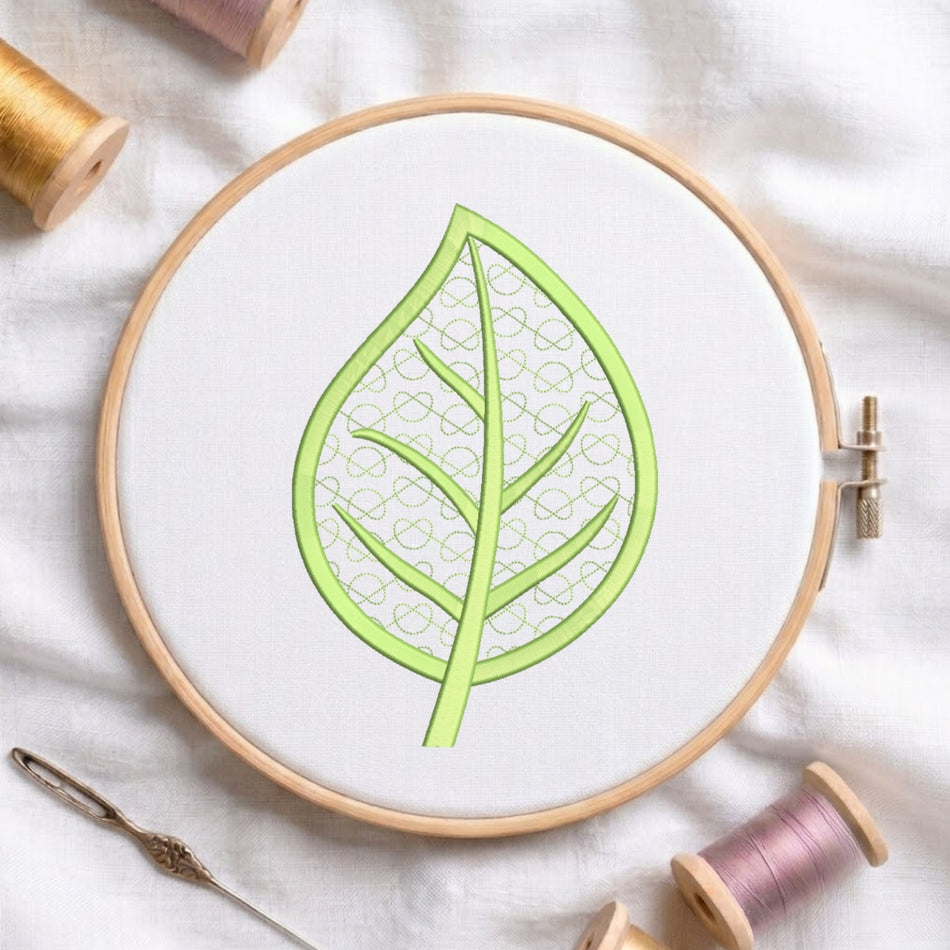 A circular embroidery hoop holding white fabric with a light green leaf design outlined and filled with a repeating pattern. The hoop is styled on a white fabric surface with spools of thread and a needle around it.