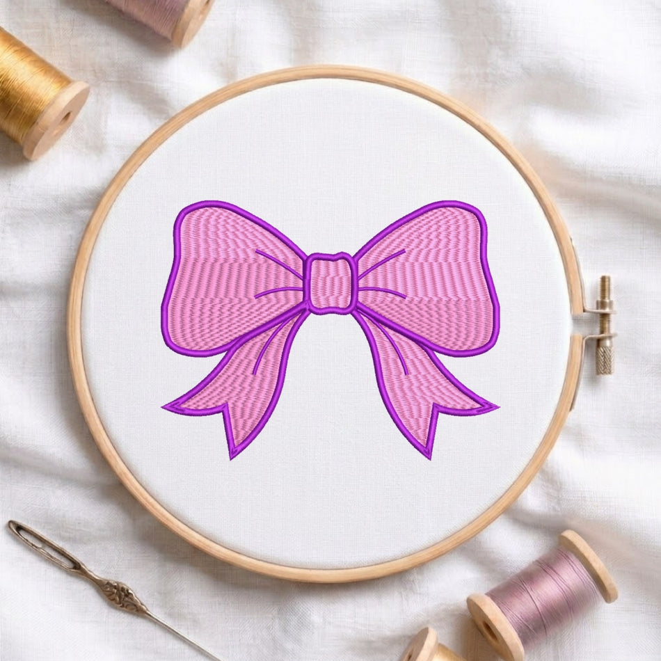 A circular embroidery hoop holding white fabric with a pink bow design outlined in purple. Spools of thread and a needle are arranged around it on a white fabric background.